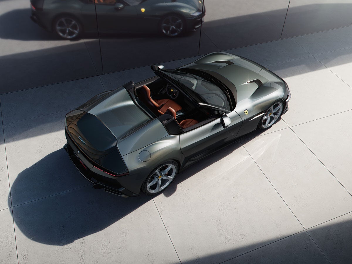 Overhead view of a metallic forest green Ferrari convertible with tan leather interior, parked on light gray tiles.