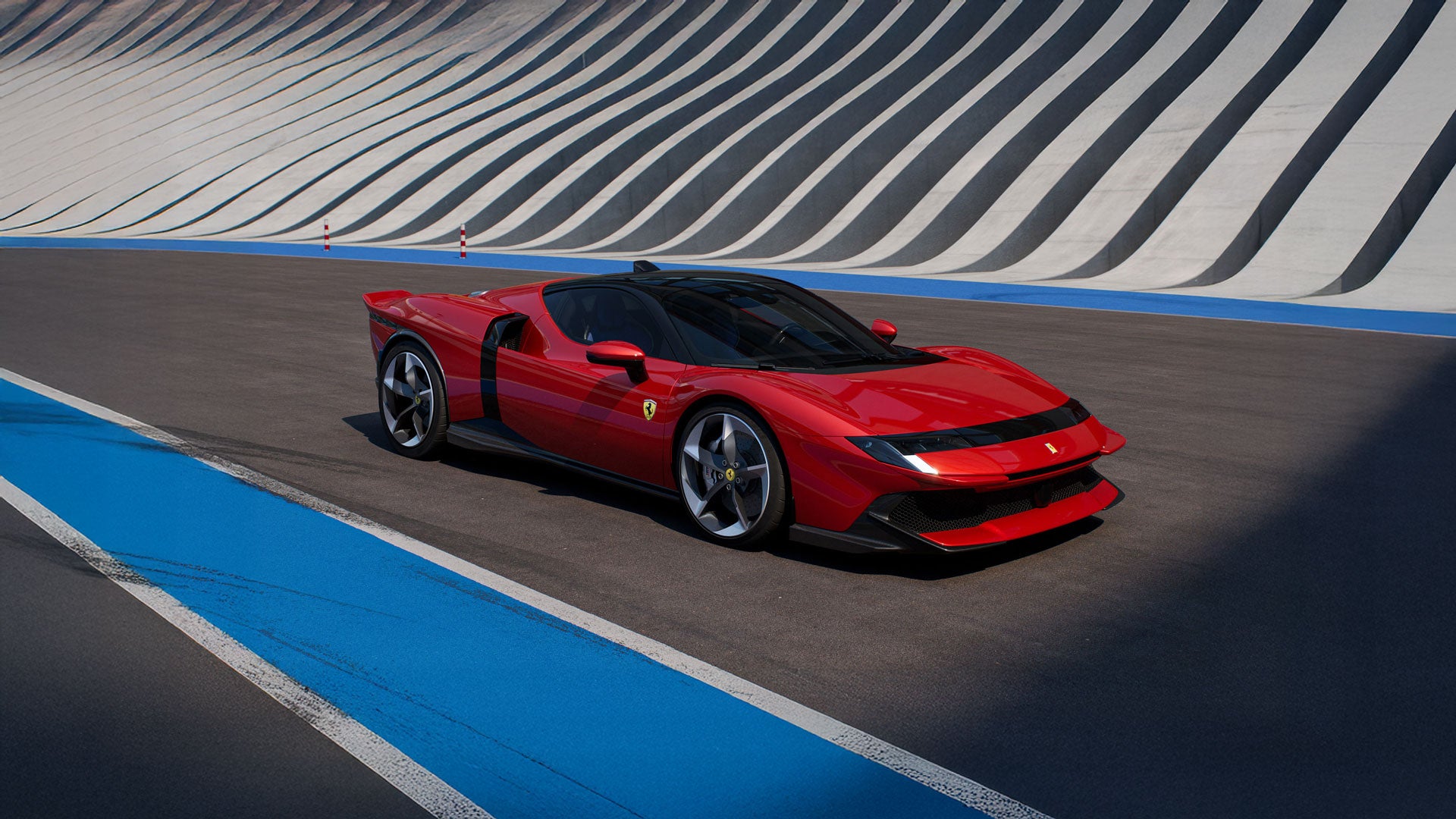 A glossy red Ferrari sits on a race track with a grey and white striped wall in the background.