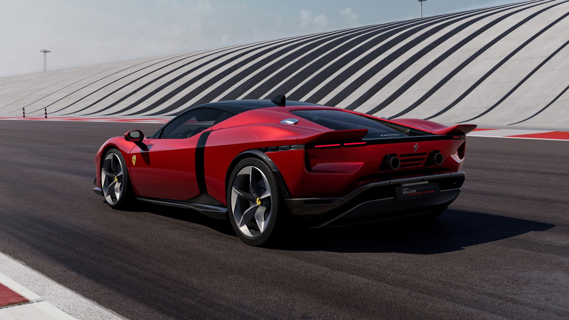 Rear view of a red Ferrari SP-8 on a racetrack with a black and white striped wall in the background.