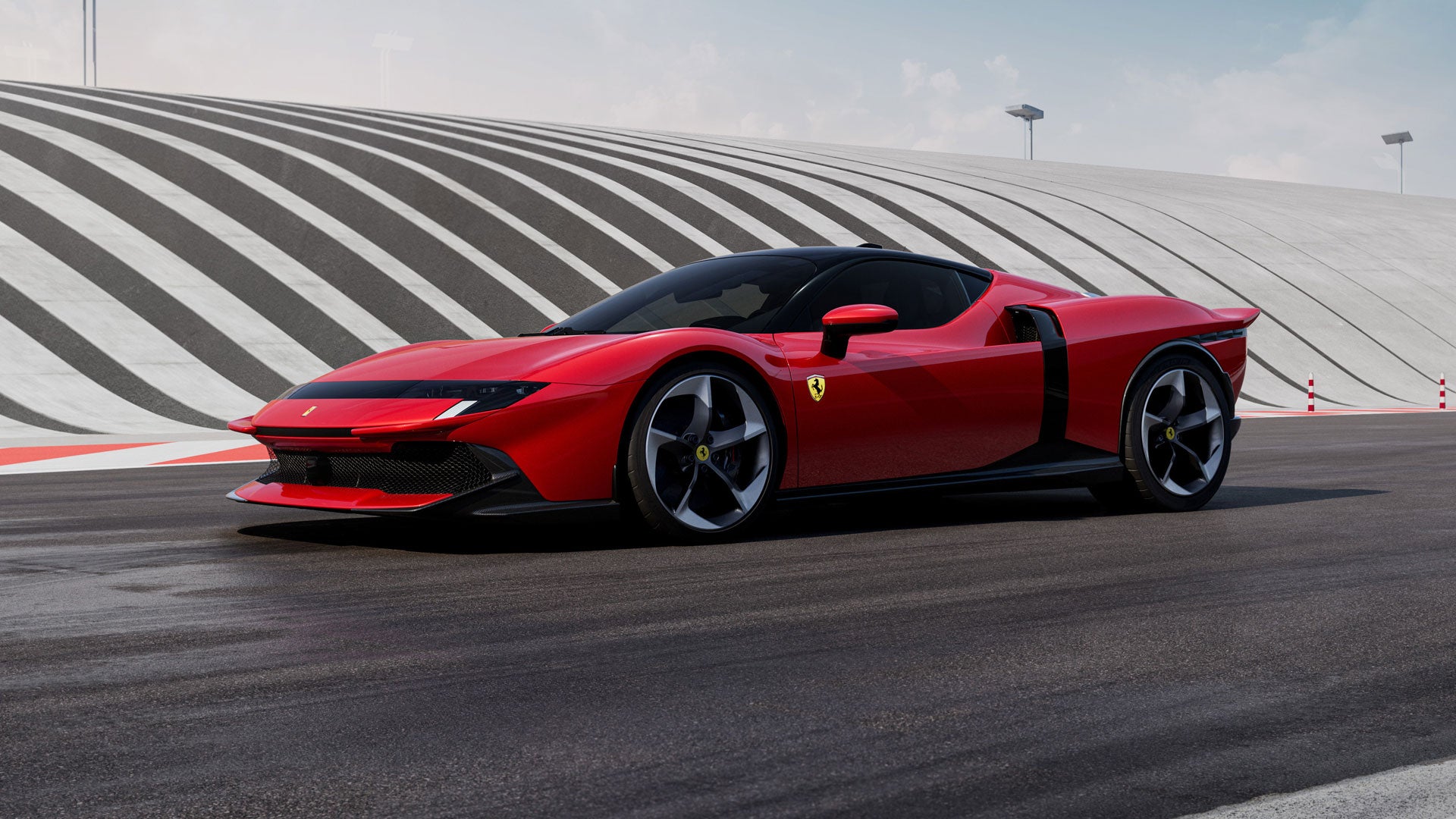 A red Ferrari sitting on a racetrack with a large, wavy, concrete structure in the background.