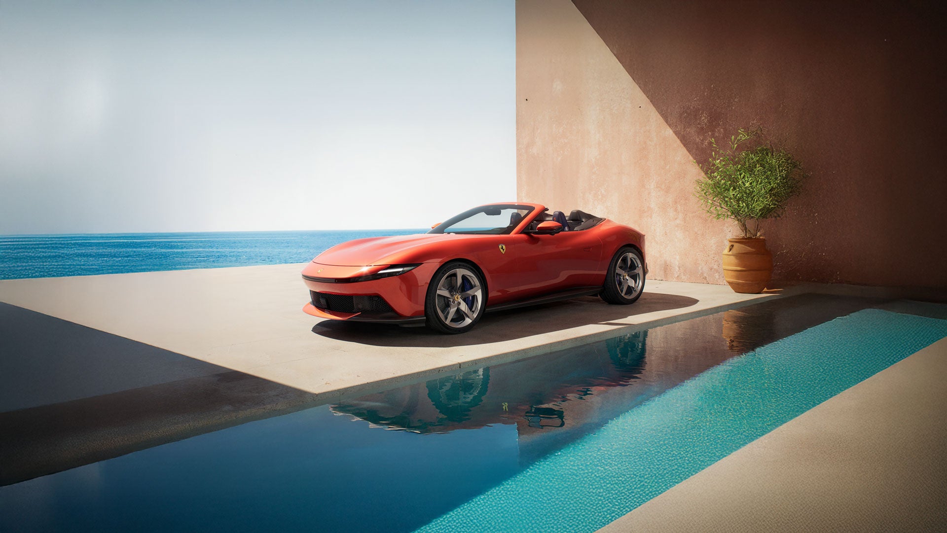 Side view of a red convertible Ferrari parked next to a turquoise swimming pool, overlooking a bright blue ocean.