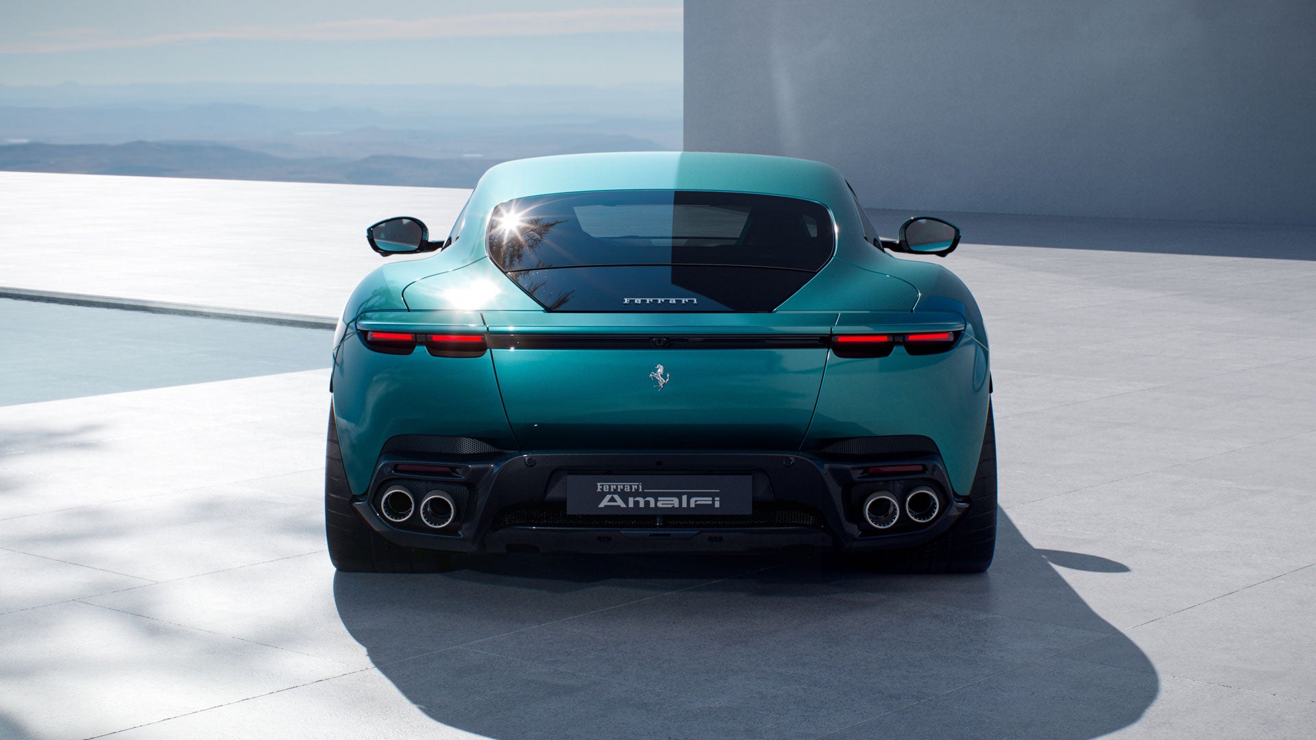 Rear view of a teal green Ferrari on a light gray surface by a pool, with mountains in the distance.