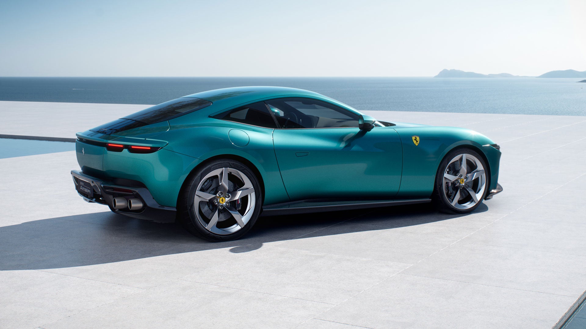 A teal Ferrari parked on a patio overlooking the ocean and distant hills.