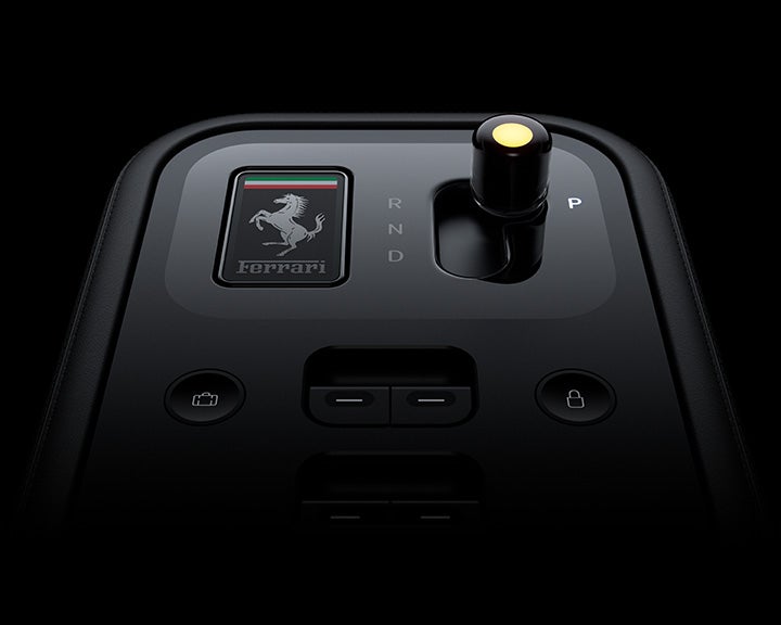Close-up of a Ferrari gear selector with an illuminated P, the Ferrari logo, and control buttons on a dark dashboard.