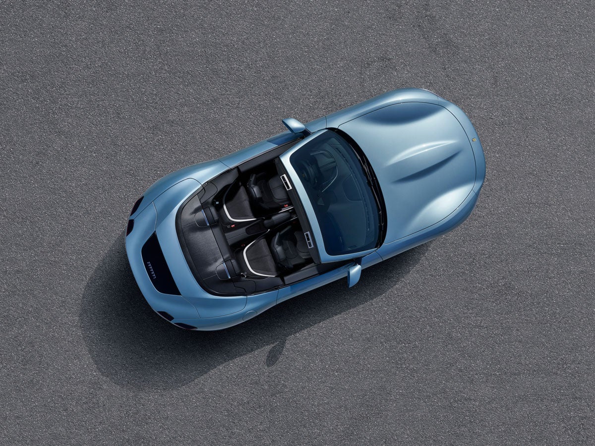 Overhead view of a light blue convertible car with black and white interior, parked on a gray asphalt surface.